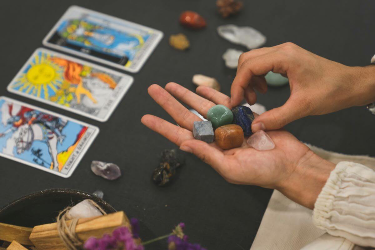 Apatit-beneficii pentru vindecarea  spirituala-piatre culori diferite asezate in palma, carti de tarot pe masa